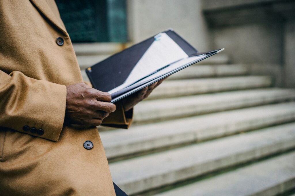 Side view of crop anonymous ethnic male executive with black folder standing on stone staircase in city