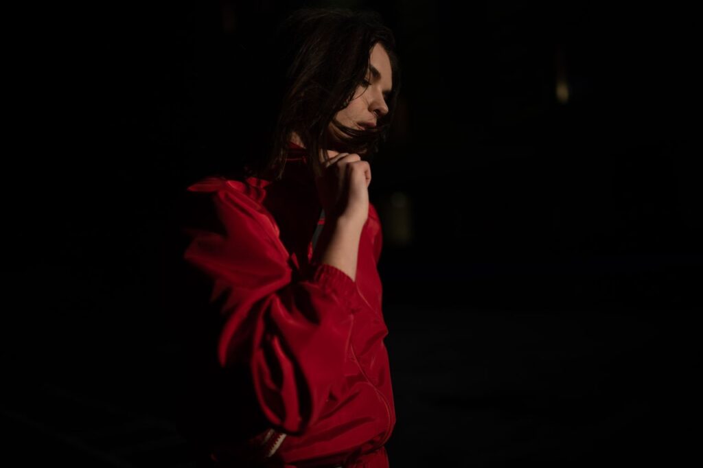 Dramatic side-view portrait of woman in a red outfit with low light and shadows.